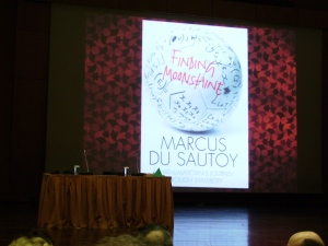 The cover of Marcus du Sautoy's new book: "Finding Moonshine: A Mathematician's Journey through Symmetry" appears on the screen in the Athens Music Hall, 22/3/2010